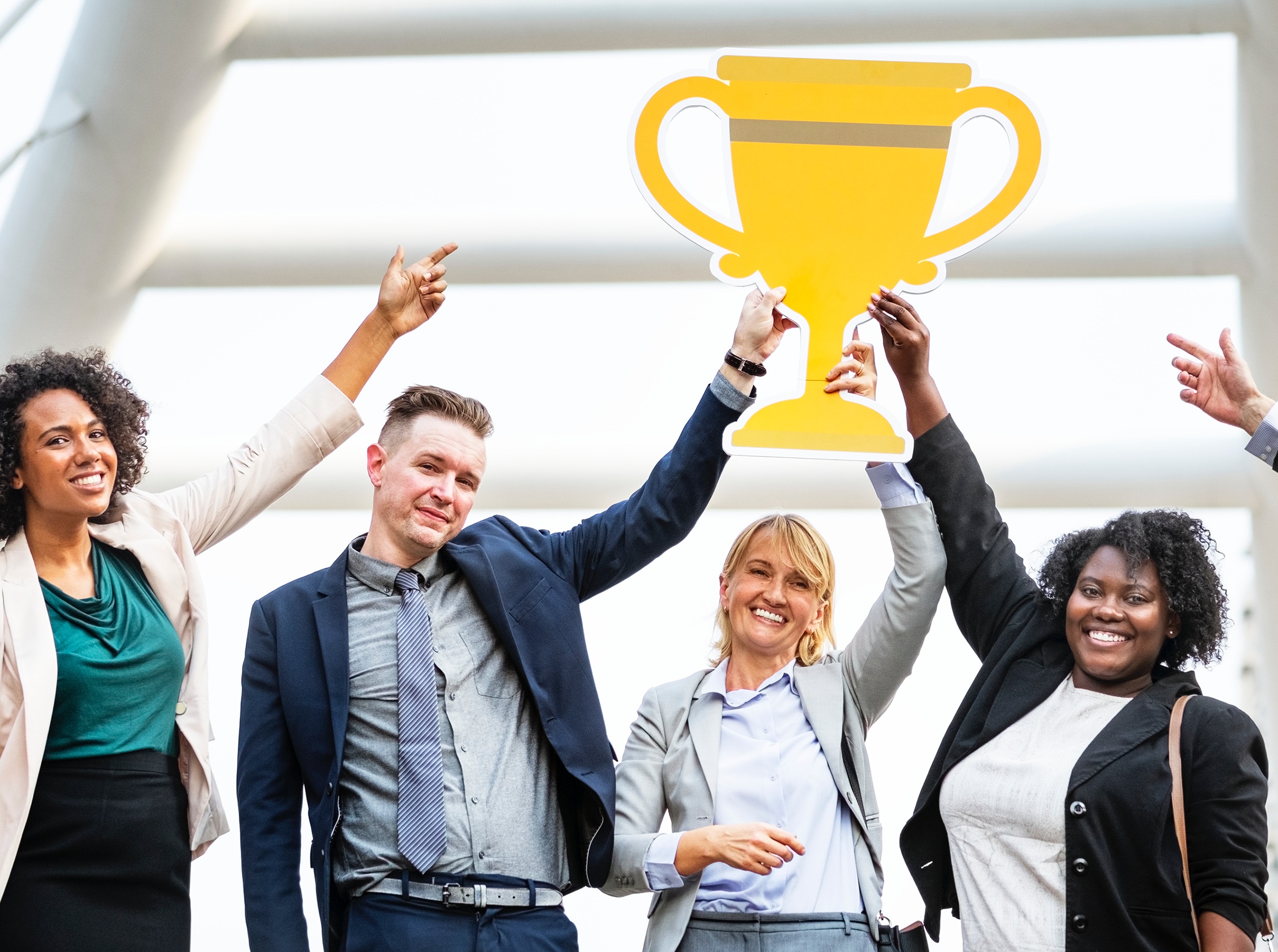  A group of people celebrate an accomplishment by holding their arms in the air and one person holds a trophy.